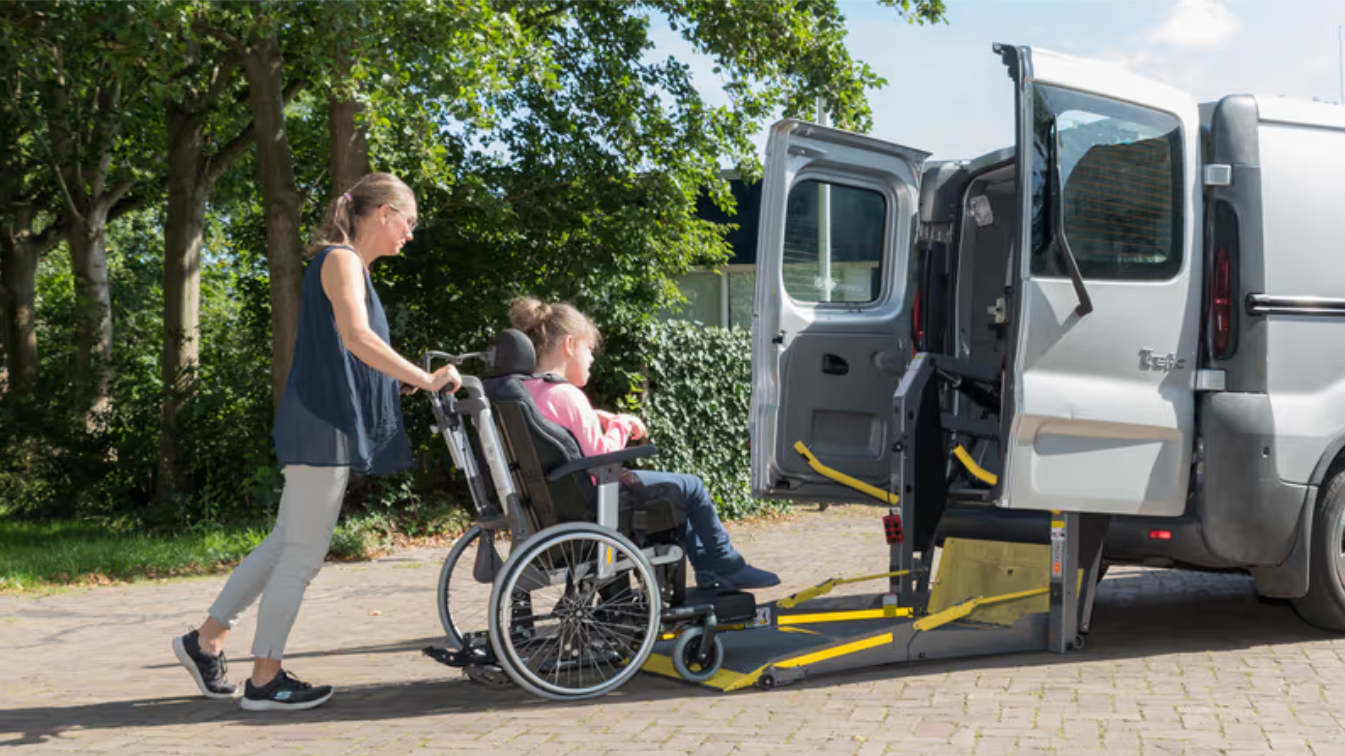 Carer assisting a young person in a wheelchair onto an accessible vehicle lift